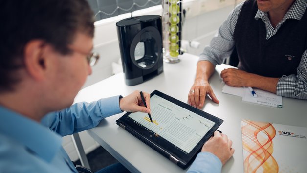 Zwei Personen sitzen sich gegenüber und schauen auf ein Tablet